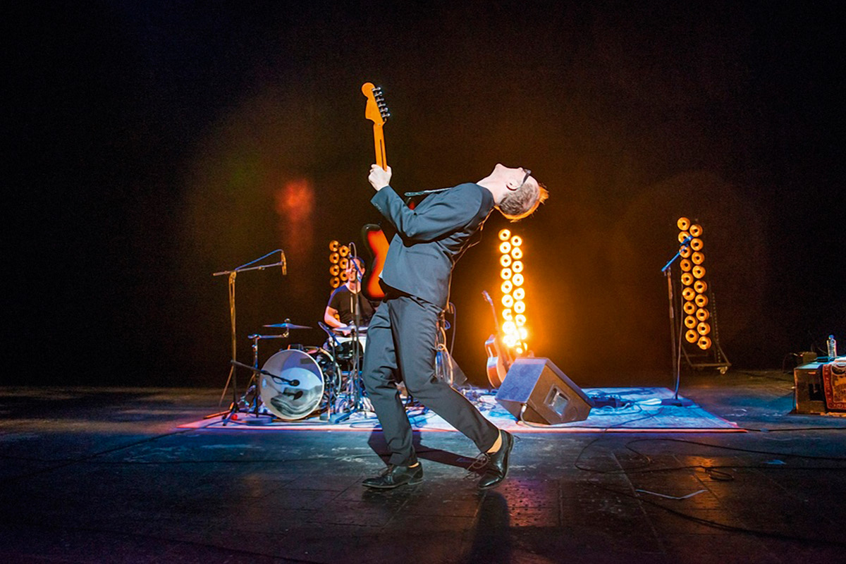 Musiker PeterLicht tanzt mit seiner Gitarre auf einer dunklen Bühne. Foto: Christian Knieps