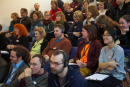Symposiums-Teilnehmer sitzen mit Kopfhörer auf der Zuschauer-Tribüne.